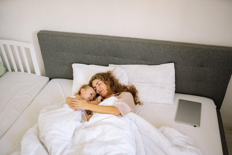 A Mother And Toddler Lying On The Bed Together