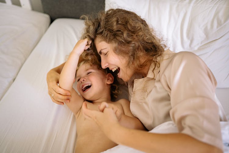 A Laughing Mother And A Toddler Lying In Bed