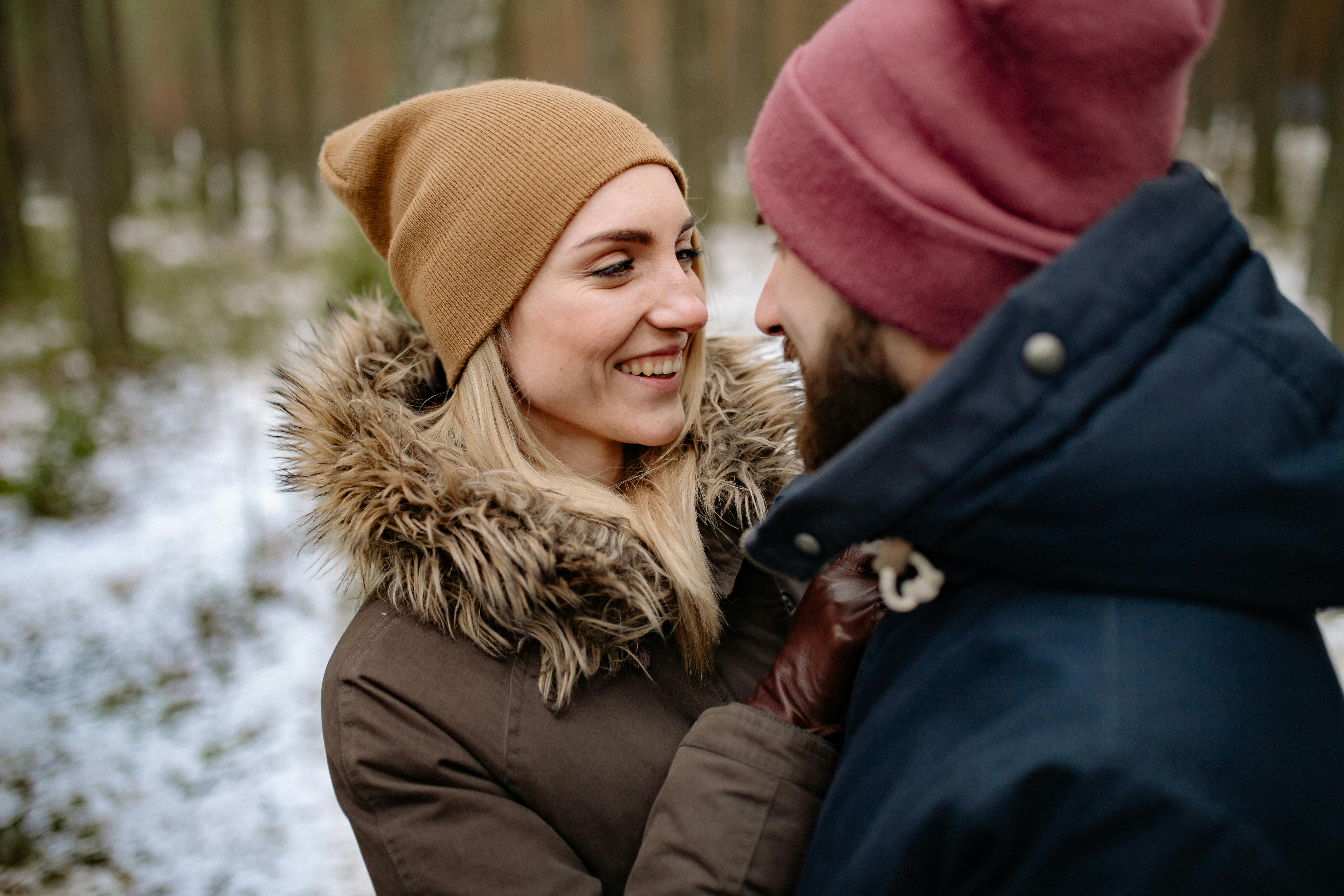一对幸福的情侣穿着冬季外套，在白雪皑皑的森林中深情相拥微笑