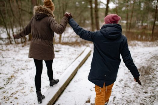 一对夫妇手牵着手，在冬季森林的雪道上保持着平衡