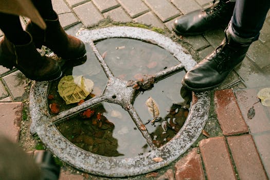 Close-up of boots around a puddle with autumn leaves on a wet street.