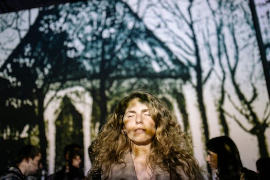 一位卷发女子闭着眼睛，站在投影的森林背景前