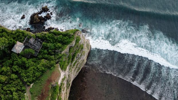 A breathtaking aerial view of a lush cliffside and ocean waves crashing below.