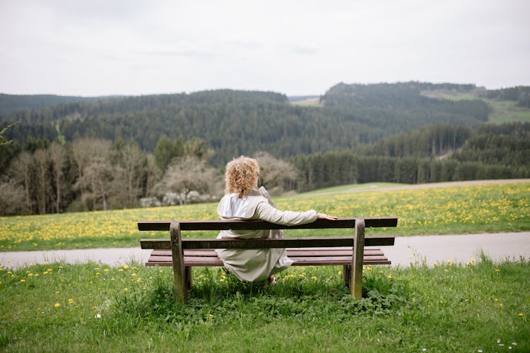 Back View Of A Woman Sitting Alone On A Wooden Bench