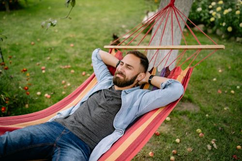 Free Bearded man in denim shirt enjoying a sunny day lying in a hammock in the garden. Stock Photo