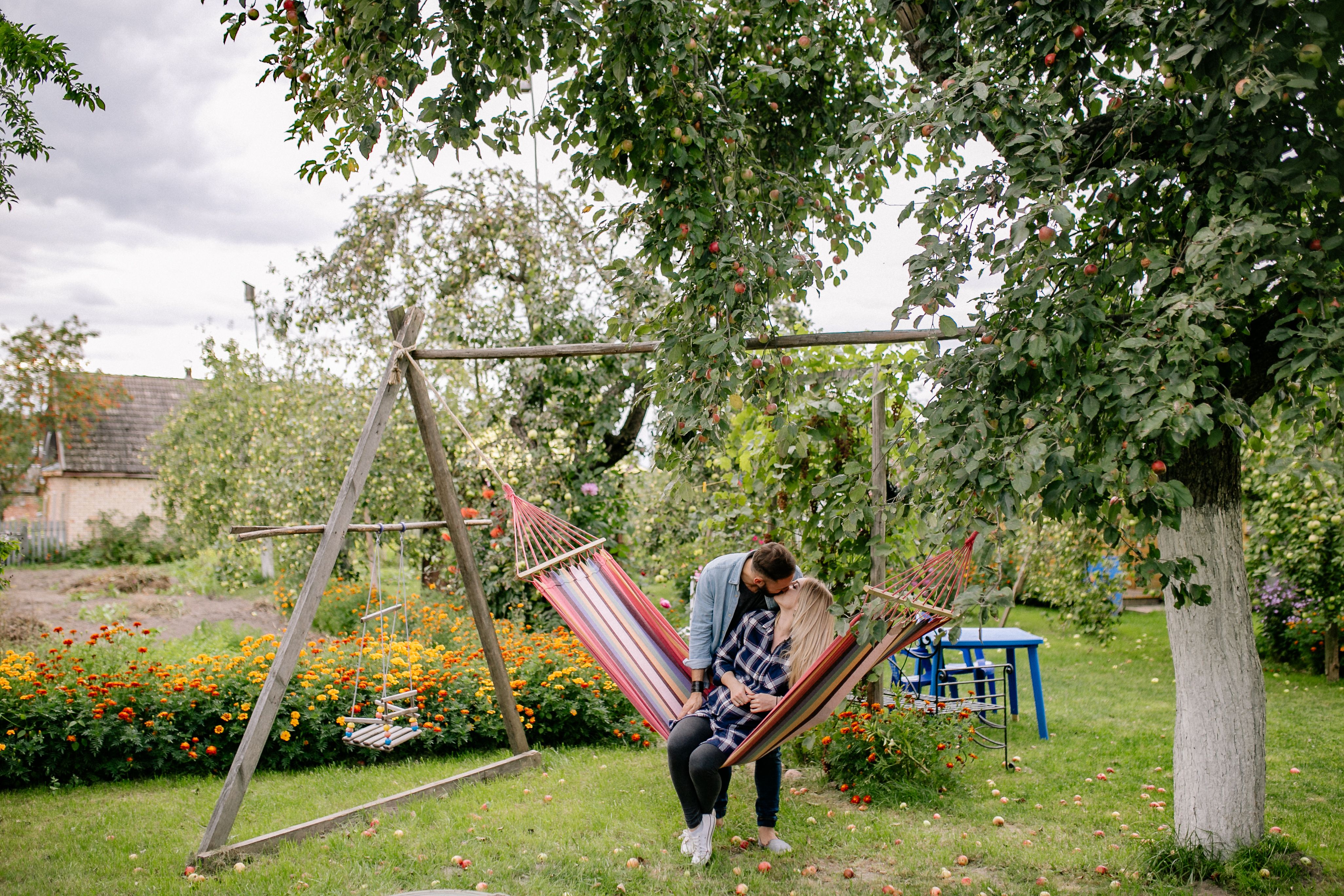 A loving couple enjoys a kiss on a hammock in a lush garden setting.