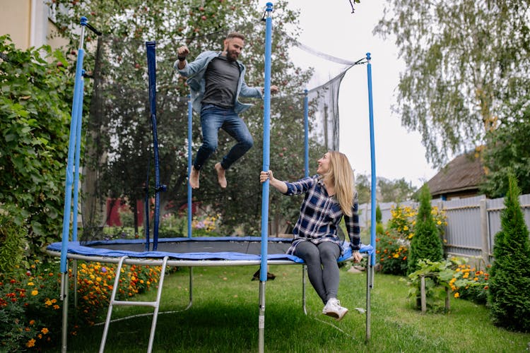 A Woman Looking At A Man Jumping On A Trampoline 