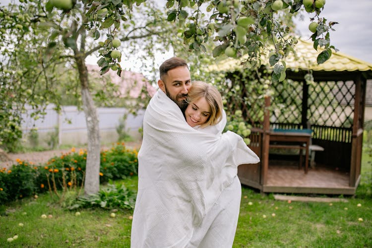 A Couple Wrapped In A White Blanket Under A Tree