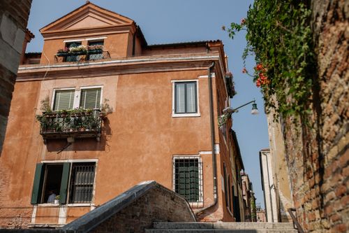 Free A warm, sunlit Venetian house with a flower-laden balcony in a quaint alley. Stock Photo