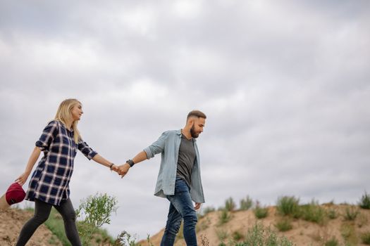 A young couple holding hands while walking outdoors under a cloudy sky.
