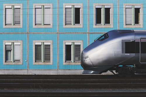 Gray Train Passing By near Blue Wall