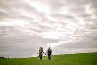 Man and Woman Walking on Green Grass Field Under White Clouds