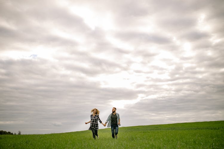 Couple Holding Hands And Running Through A Field 