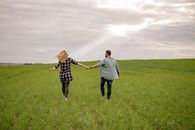 Man and Woman Holding Hands While Walking on Green Grass Field