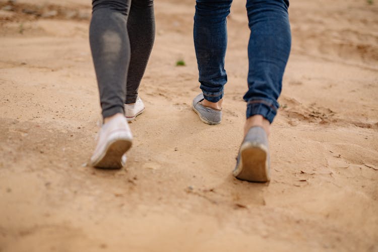 Close-up Of Couple Legs Walking On Sand