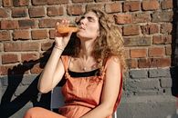 Woman Leaning on a Brick Wall and Drinking Juice out of a Bottle