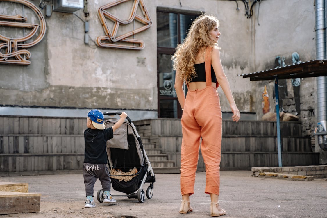 Woman in Orange Pants Standing beside a Boy Holding Stroller