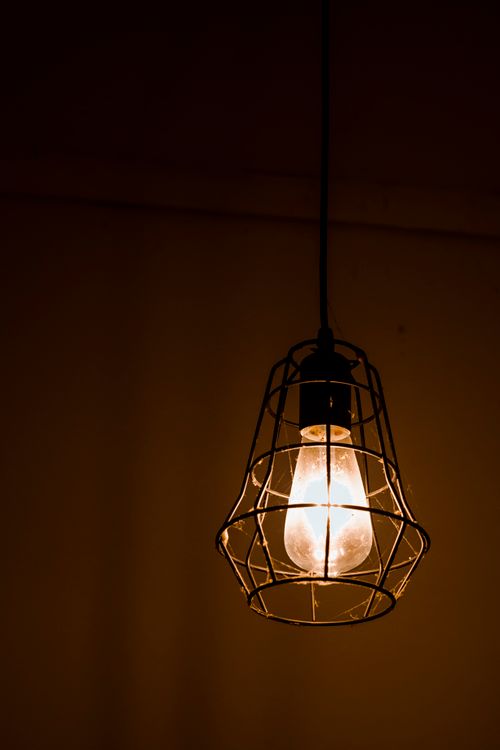 Free Low angle of stylish pendant lamp with light bulb in metal net in dark room Stock Photo