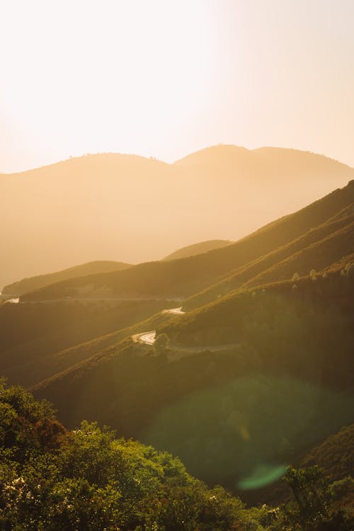 Spectacular scenery of vast hilly terrain with narrow serpentine road under bright sunlight in early evening