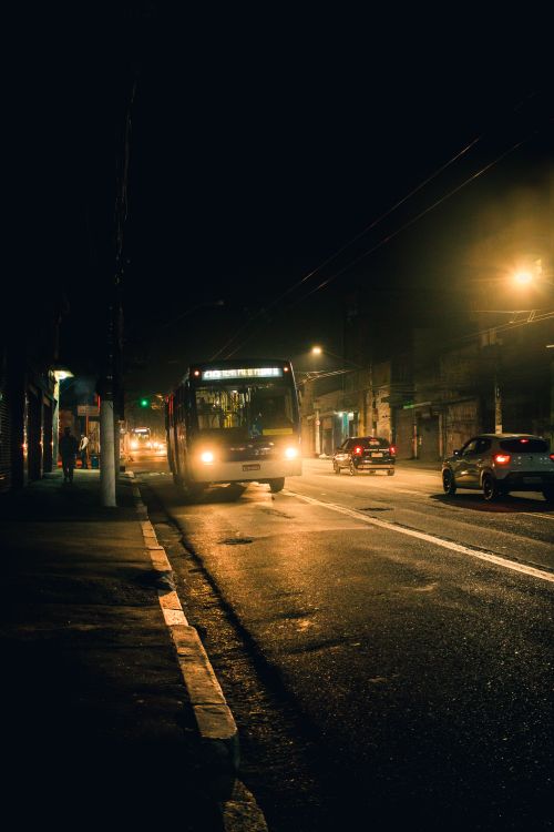 Free Bus with glowing headlights riding on shabby asphalt road alongside sidewalk under trolley wires Stock Photo