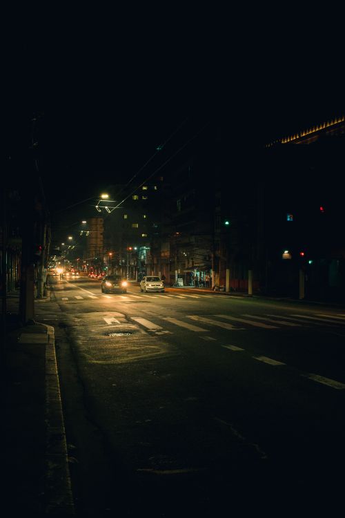 Free Vehicles driving on night street with shabby asphalt pavement and crosswalks illuminated by lights from trolley wires Stock Photo