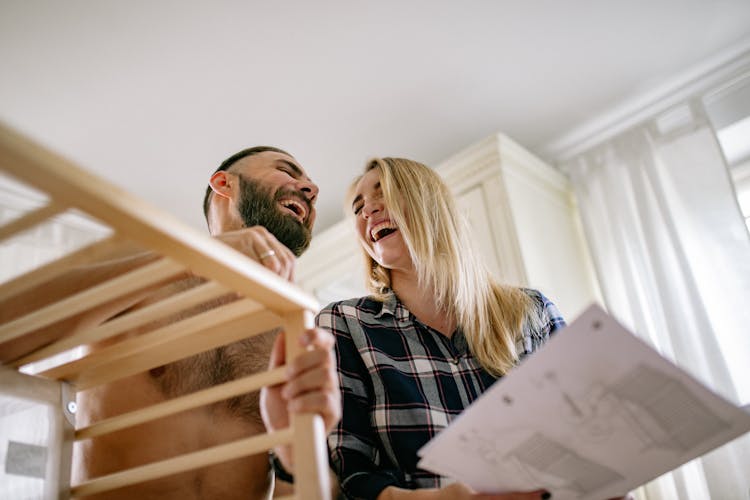 Man And Woman Building A Baby Crib And Laughing 