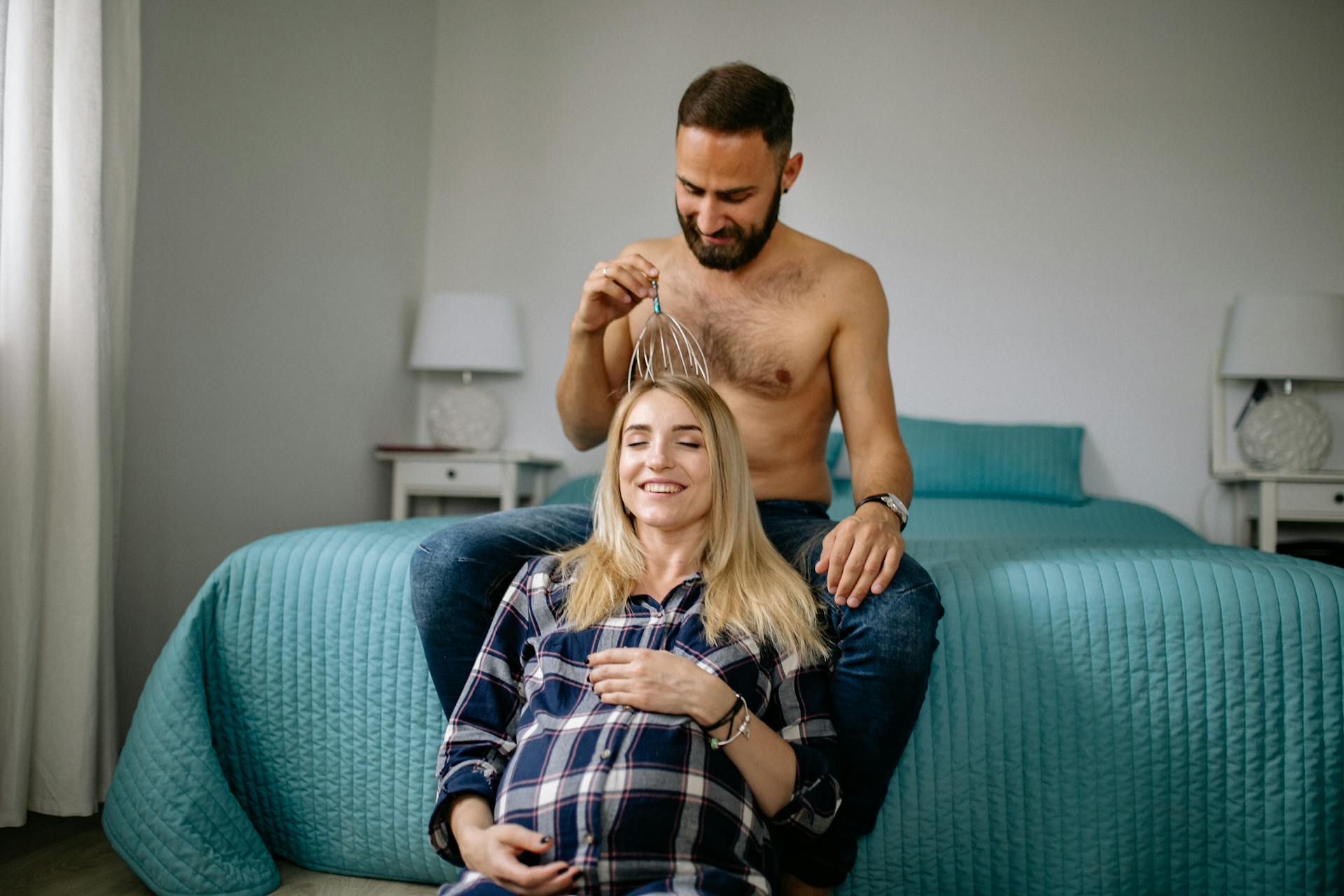 Happy couple enjoying a relaxing moment indoors. Man massaging pregnant woman's head.