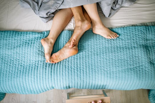 Top view of a couple's feet intertwined on a bed with a blue quilt. Intimate and cozy setting.