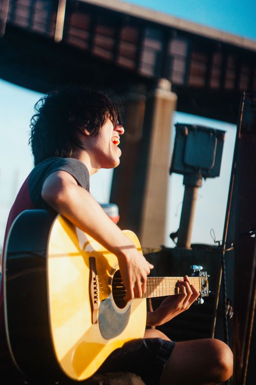 Free A young man passionately plays an acoustic guitar outdoors in sunlight. Stock Photo