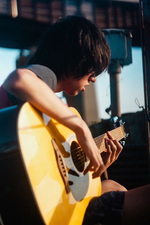 Free A teenager intently playing an acoustic guitar outdoors with selective focus on the instrument. Stock Photo
