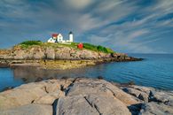 White and Red Lighthouse on Brown Rocky Mountain Near Body of Water