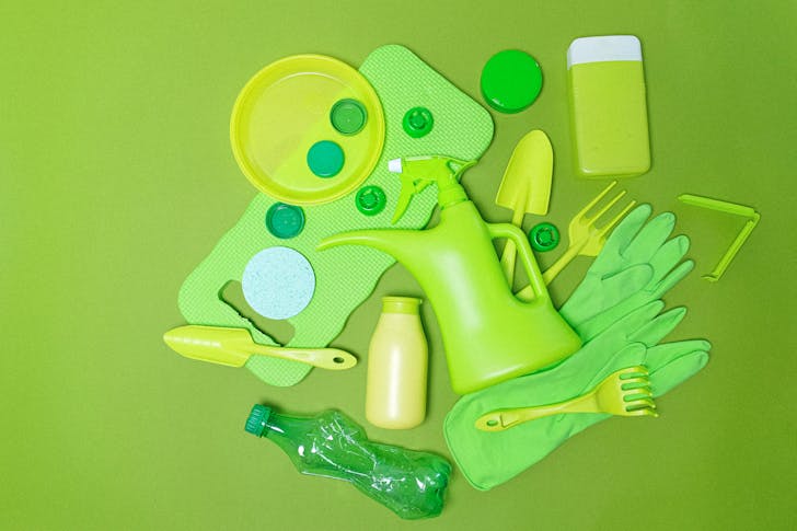Top view monochrome of various plastic bottles and kitchen utensil polluting planet on green background