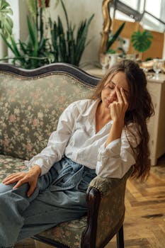 A woman relaxes on a floral vintage sofa in a cozy, light-filled room with plants.