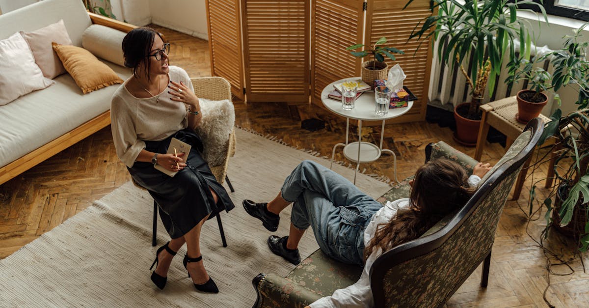 Two women engaged in a psychotherapy session in a warm, inviting interior with plants and natural lighting.