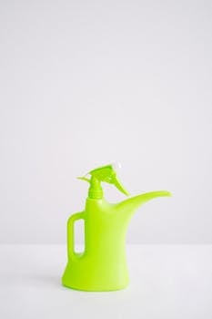 Green plastic reusable bottle for liquid intended for watering and spraying plants on white background
