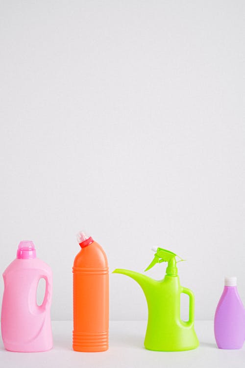 Collection of colorful bottles of detergent and cleaning supplies placed in row on table against white background in light room