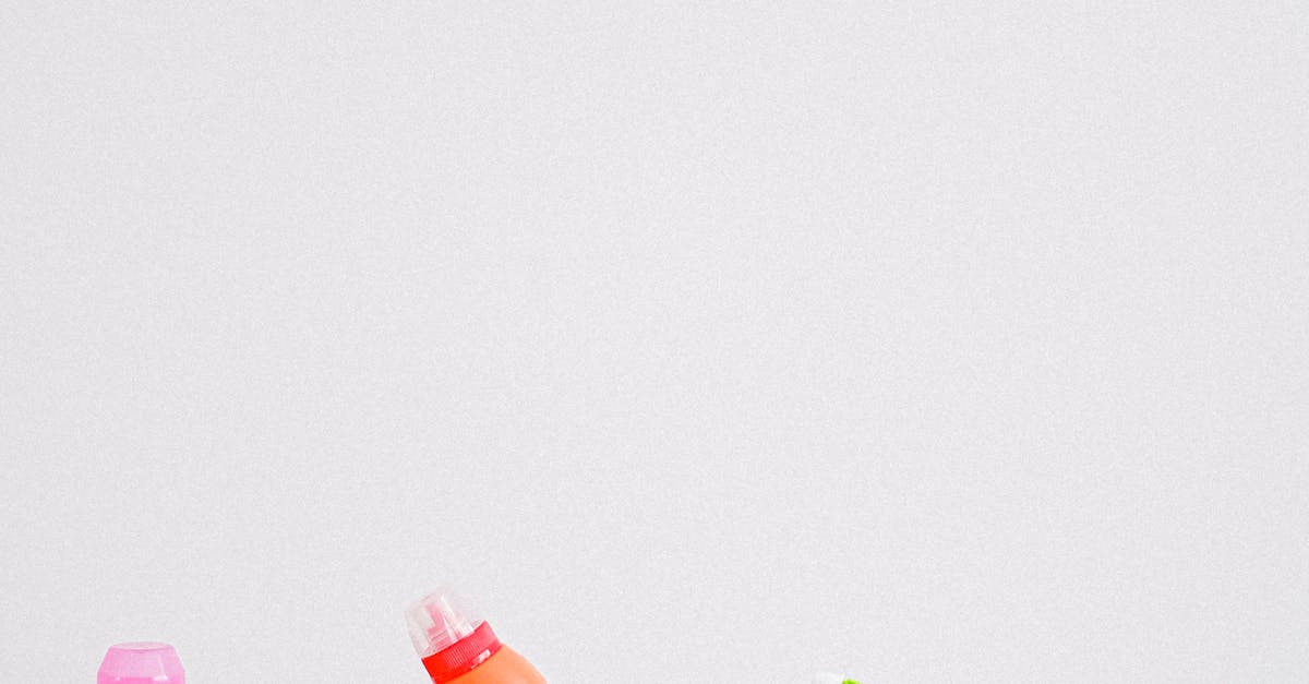 Collection of colorful bottles of detergent and cleaning supplies placed in row on table against white background in light room