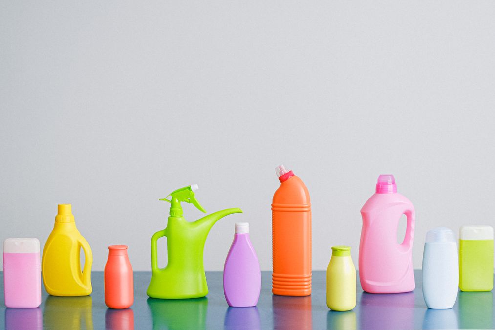 Frascos coloridos de produtos de limpeza organizados lado a lado sobre uma superfície clara