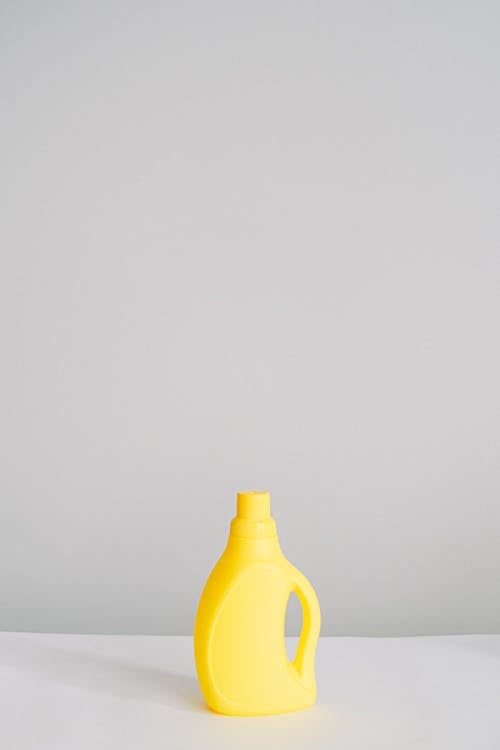 Yellow plastic bottle with antibacterial chemical liquid for household routine placed on table isolated on white background in light room