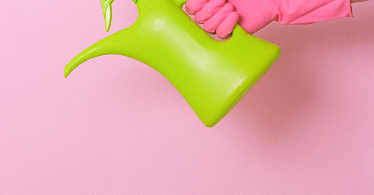 Unrecognizable person with pink latex glove with little refillable watering can with dispenser in hand on pink background in studio