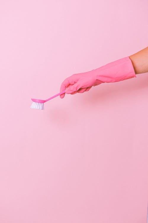 Free Unrecognizable cleaner wearing protective glove using plastic brush in hand to remove dirt during household against pink background in studio Stock Photo