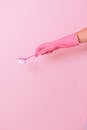 Unrecognizable cleaner wearing protective glove using plastic brush in hand to remove dirt during household against pink background in studio