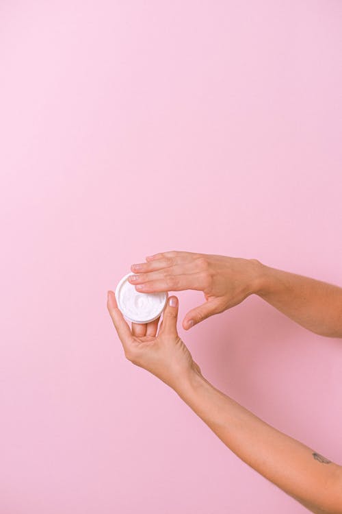 Unrecognizable person with jar of cosmetic product for skin care in hand on pink background in studio