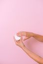 Unrecognizable person with jar of cosmetic product for skin care in hand on pink background in studio