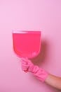 Crop anonymous person in pink rubber glove showing pink plastic dust shovel in light studio