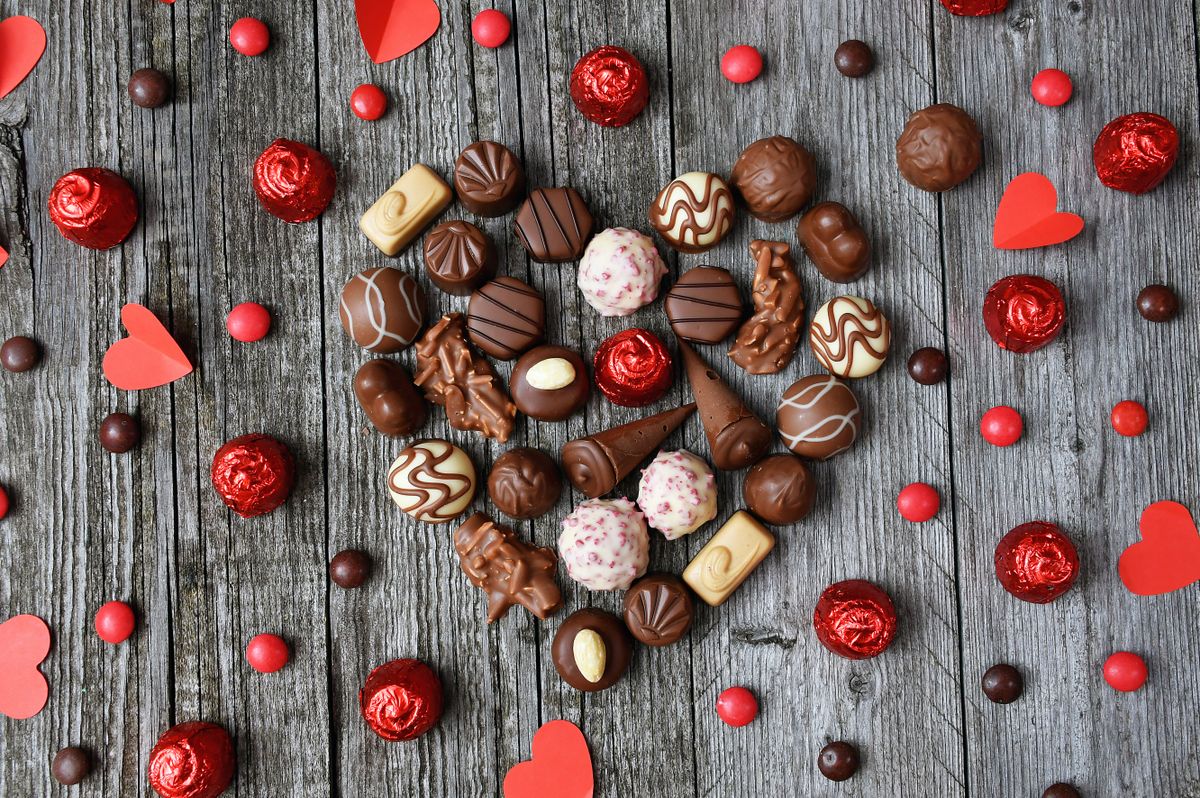 Assorted chocolates arranged in a heart shape on weathered wooden planks with red accents, perfect for romantic themes.