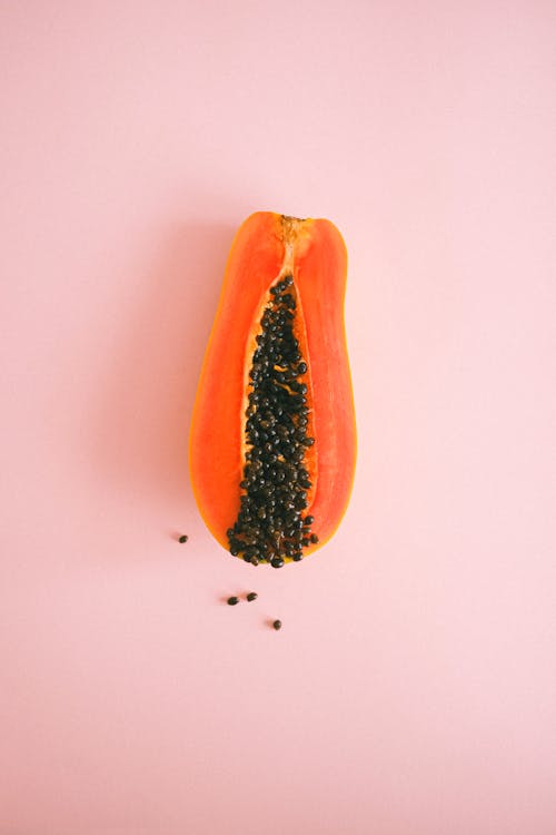 Cut ripe exotic papaya fruit on pink surface