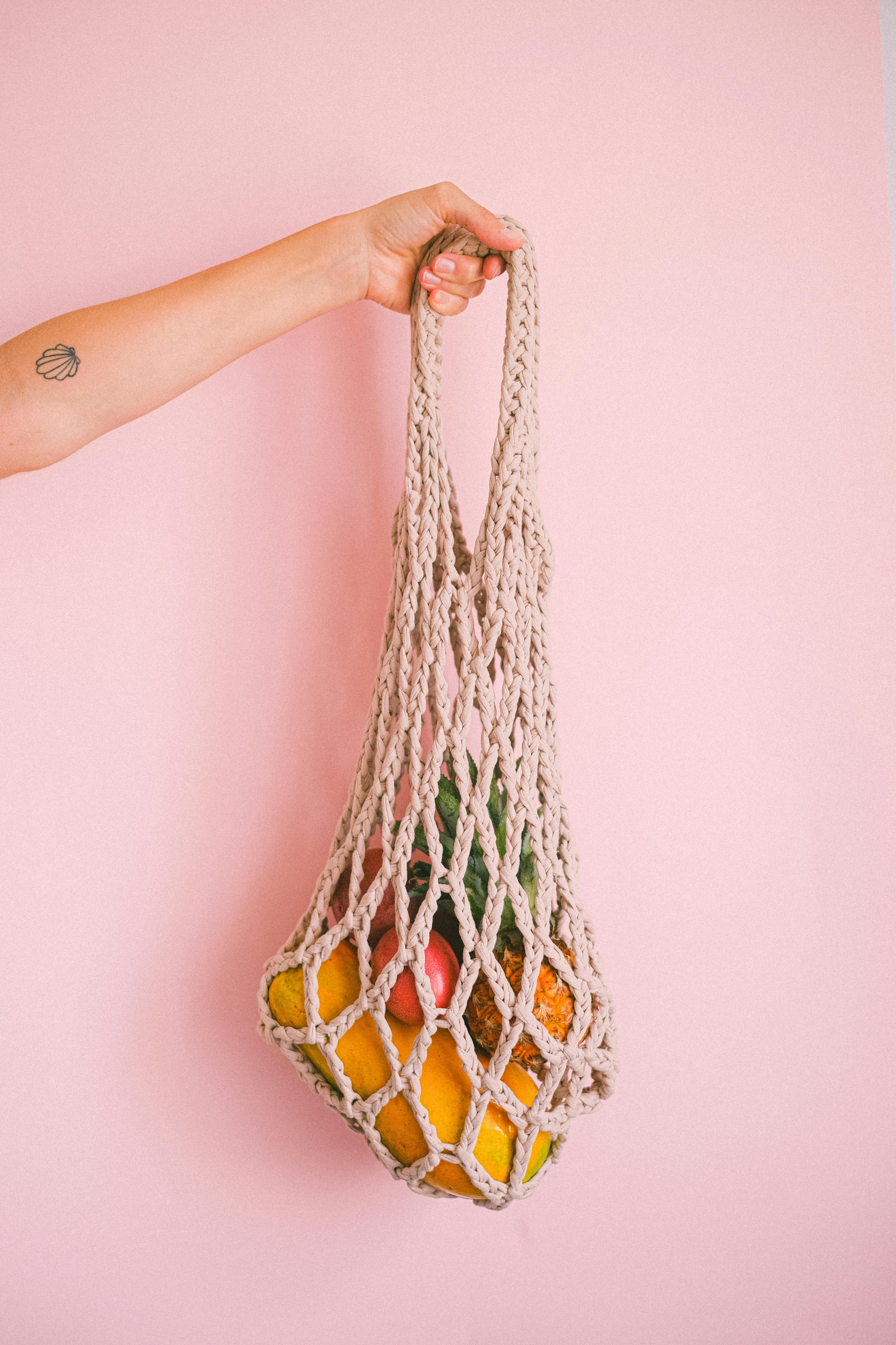 crop faceless person holding net bag with exotic fruits