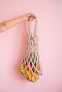 Crop faceless person holding net bag with exotic fruits