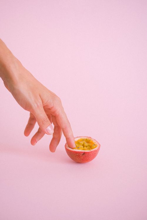 Free Crop unrecognizable female touching gently half of ripe juicy passion fruit placed on pink surface in studio Stock Photo